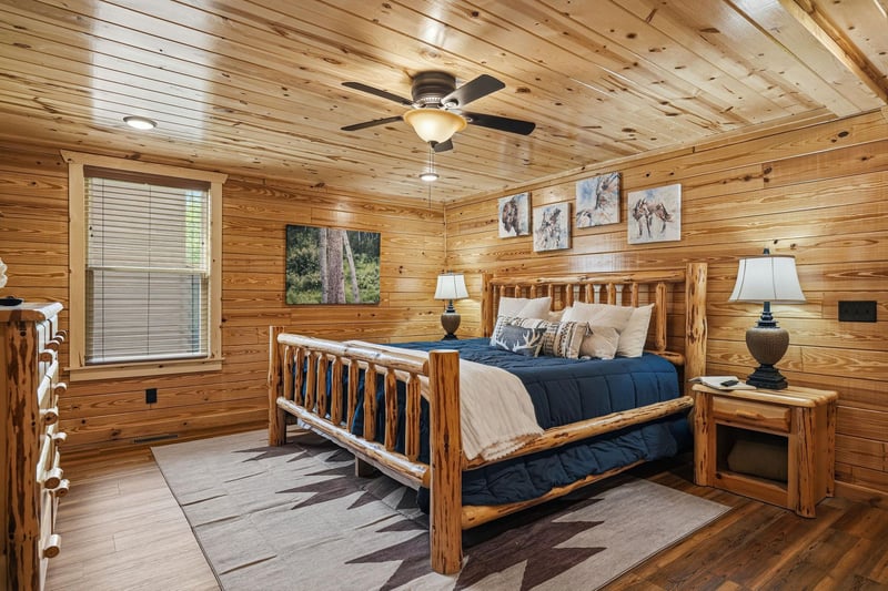 Sink into your cozy log bed beneath rustic wood walls and wildlife art, where a gentle ceiling fan keeps your retreat comfortable and welcoming.