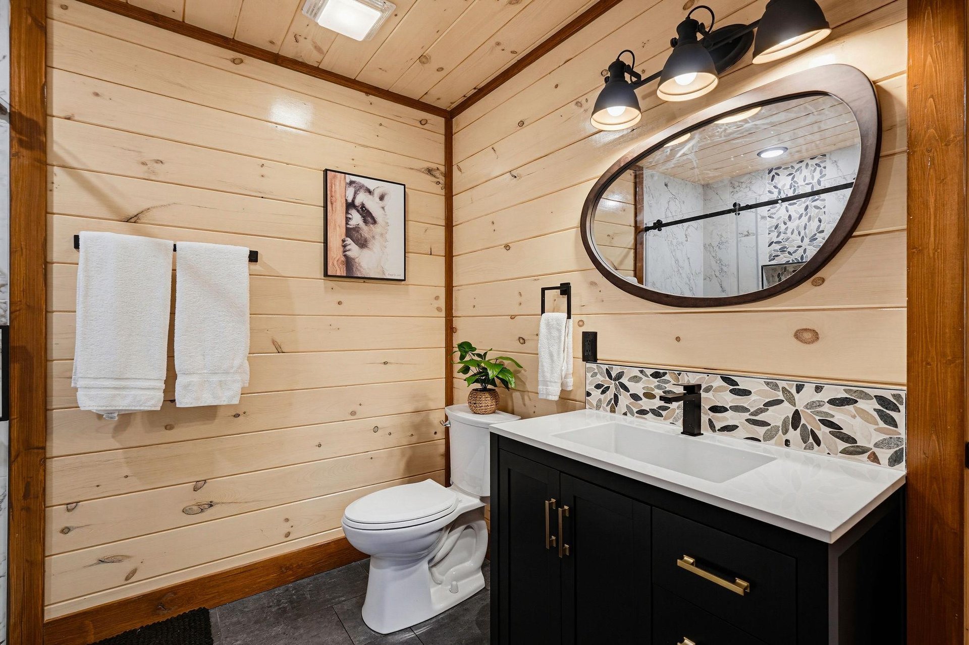 Step into a beautifully designed bathroom featuring warm shiplap walls, elegant pebble tile accents, and modern fixtures. Fresh towels await your arrival in this inviting, spalike space.
