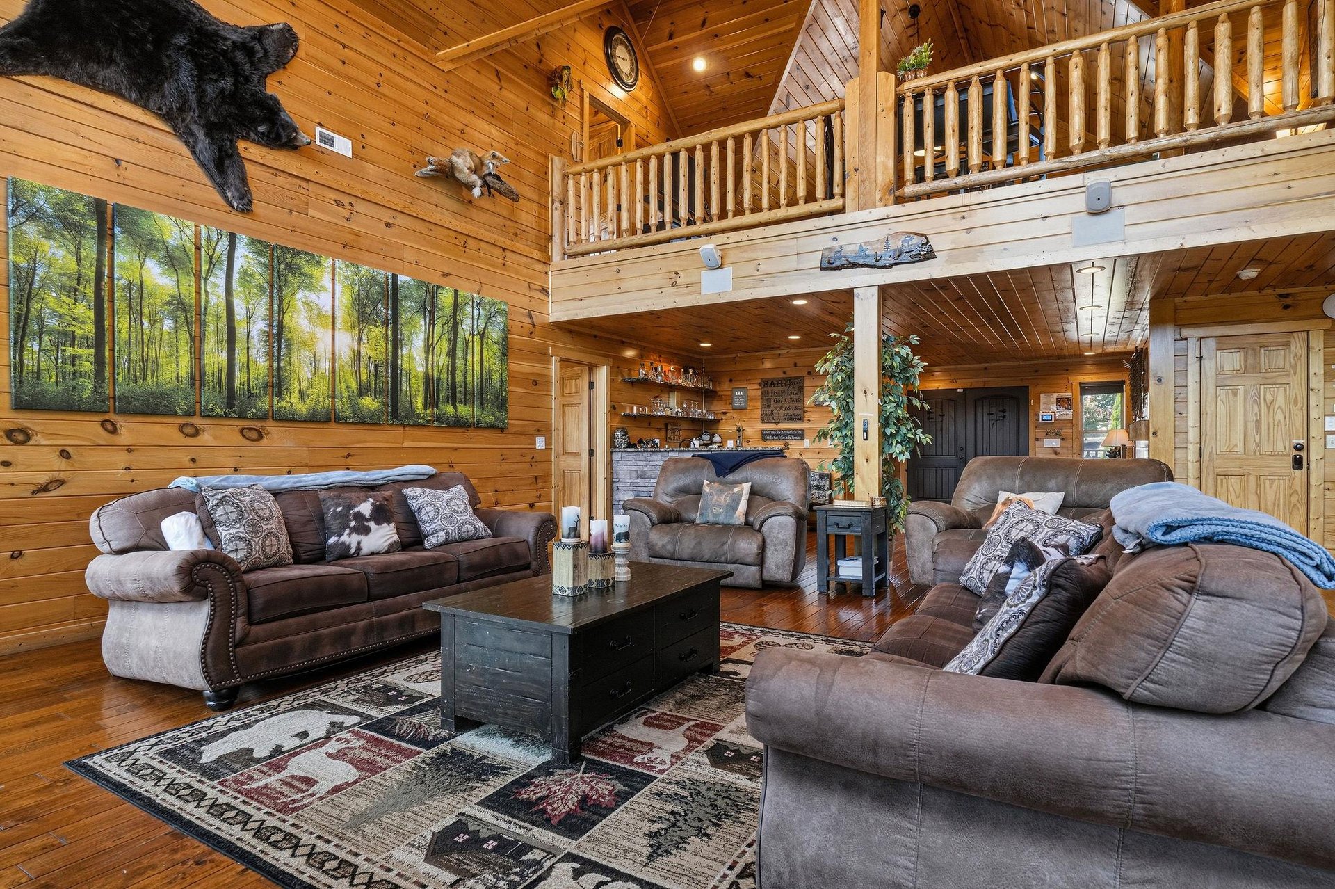Sink into plush seating beneath soaring cathedral ceilings in your spacious cabin living room, where rustic wood beams, wildlife accents, and a cozy loft create your perfect mountain retreat.