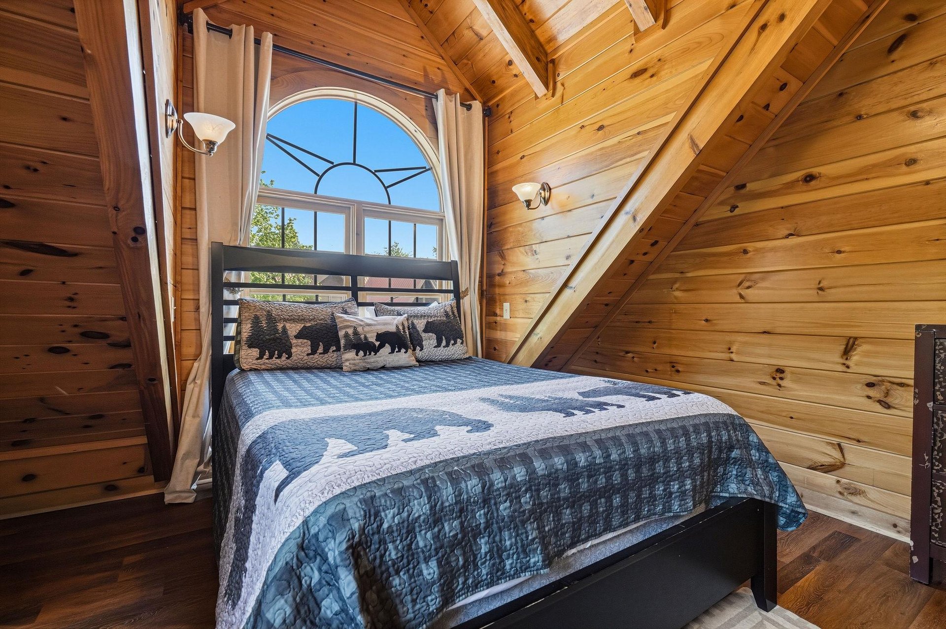 Rest peacefully in this cozy loft bedroom, where rustic wood beams frame your woodland dreams and an arched window welcomes morning light.