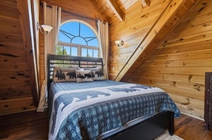 Rest peacefully in this cozy loft bedroom, where rustic wood beams frame your woodland dreams and an arched window welcomes morning light.