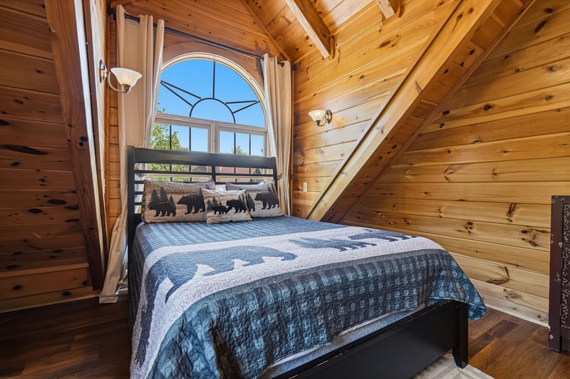 Rest peacefully in this cozy loft bedroom, where rustic wood beams frame your woodland dreams and an arched window welcomes morning light.