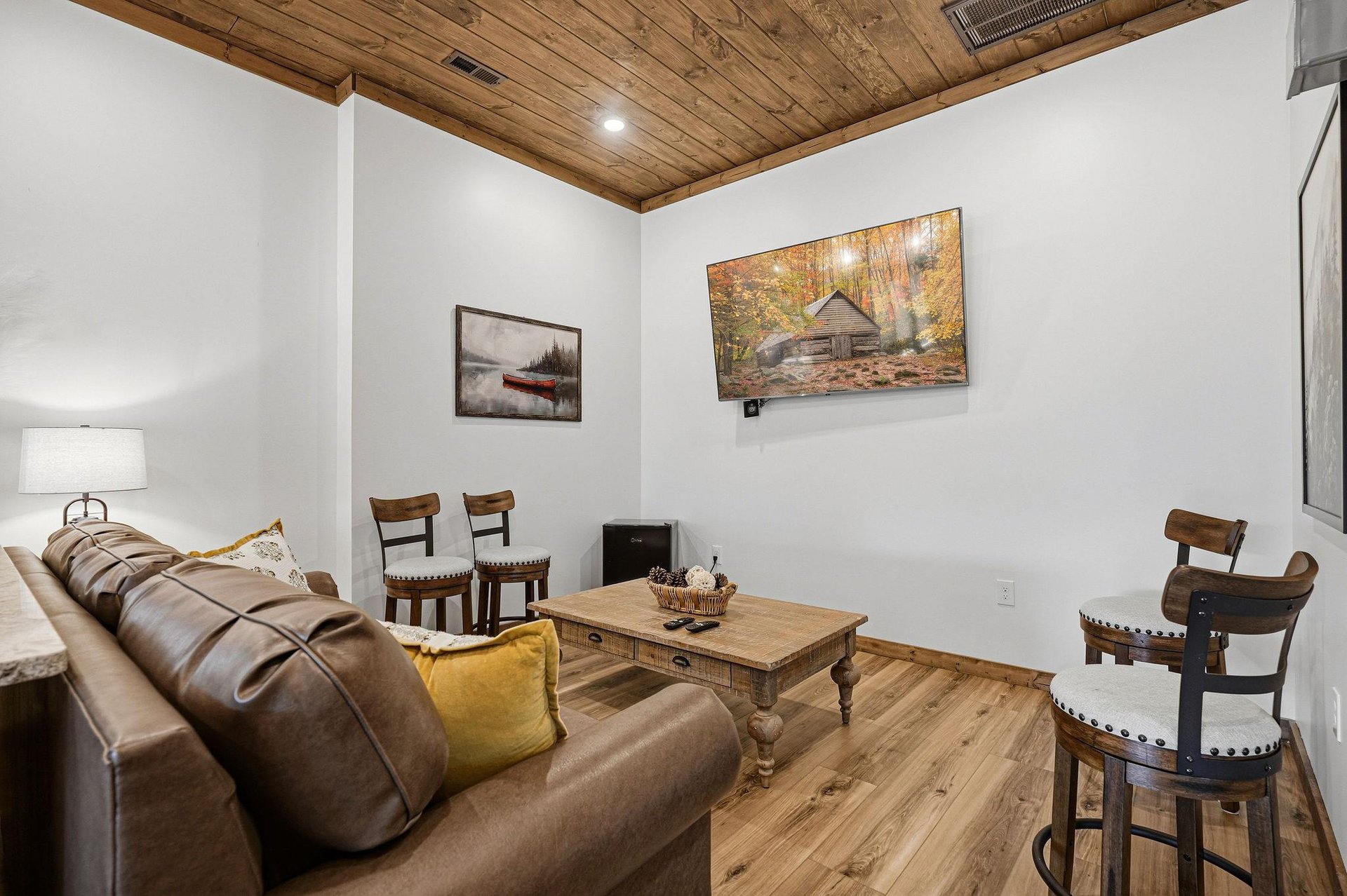 Unwind in your cozy living space featuring rustic wood ceilings, plush leather seating, and charming cabin artwork that creates the perfect retreat atmosphere.