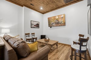 Unwind in your cozy living space featuring rustic wood ceilings, plush leather seating, and charming cabin artwork that creates the perfect retreat atmosphere.