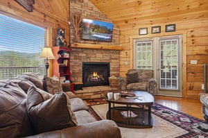 Curl up on plush sofas and warm yourself by the crackling stone fireplace in this inviting cabin living room, complete with vaulted wood ceilings and natural light streaming through the windows.