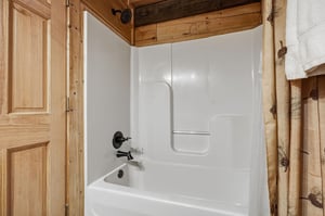 Unwind in your private bathtub surrounded by warm rustic wood finishes and charming pinecone accents that create a cozy mountain retreat atmosphere.