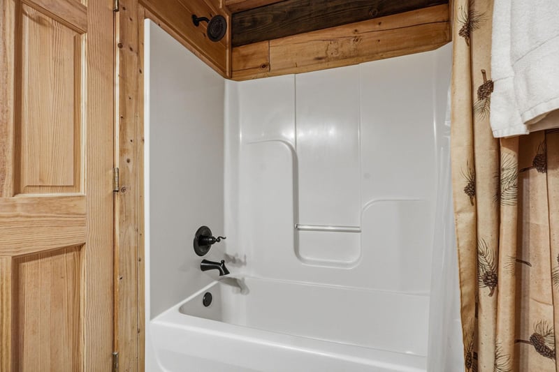 Unwind in your private bathtub surrounded by warm rustic wood finishes and charming pinecone accents that create a cozy mountain retreat atmosphere.