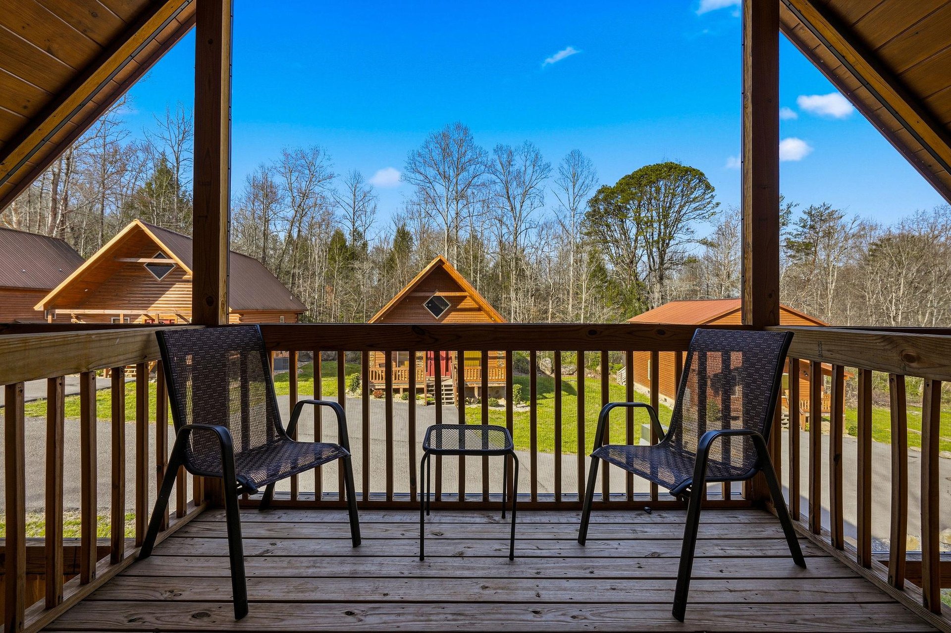 Step onto your private balcony for peaceful moments overlooking charming cabins nestled among towering trees under bright blue skies.