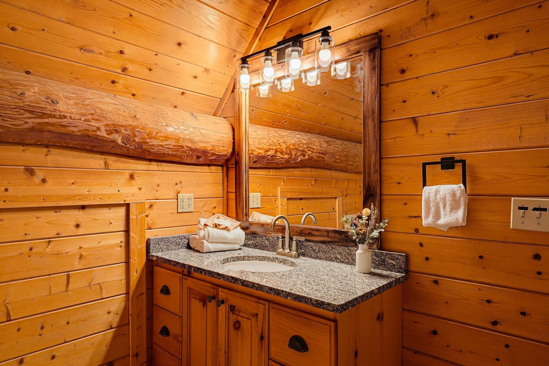 Step into this cozy bathroom with warm wood paneling, elegant granite countertop, and soft lighting that creates a welcoming mountain retreat atmosphere.