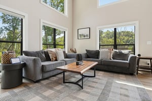 Settle into this bright, airy living space where towering windows frame lush treetop views. Your perfect spot to unwind with morning coffee or gather for an evening in.