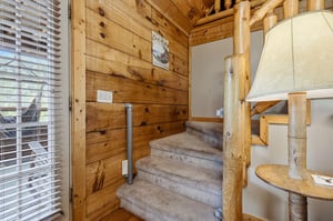 Rustic log railings guide you upstairs through warm woodpaneled walls, blending cozy cabin charm with comfort at every step.