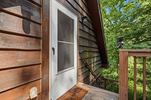 Rustic charm meets serene nature at this cabin entrance, where the weathered wood and treetop canopy welcome your peaceful forest escape.