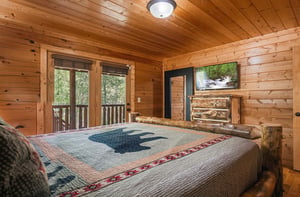 Drift off surrounded by warm wood walls and nature views from your private balcony in this cozy cabin bedroom.