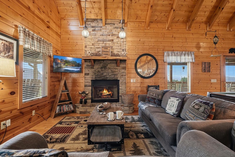 Unwind in your cozy living room with vaulted pine ceilings, a glowing stone fireplace, and rustic cabin charm that makes you feel right at home.