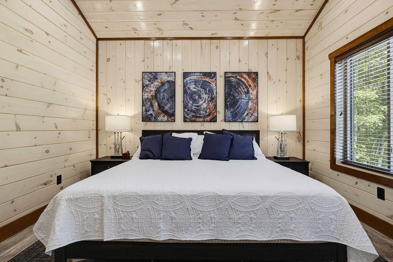 Slip into crisp white linens and let the peaceful woods outside your window lull you to sleep in this serene cabin bedroom.