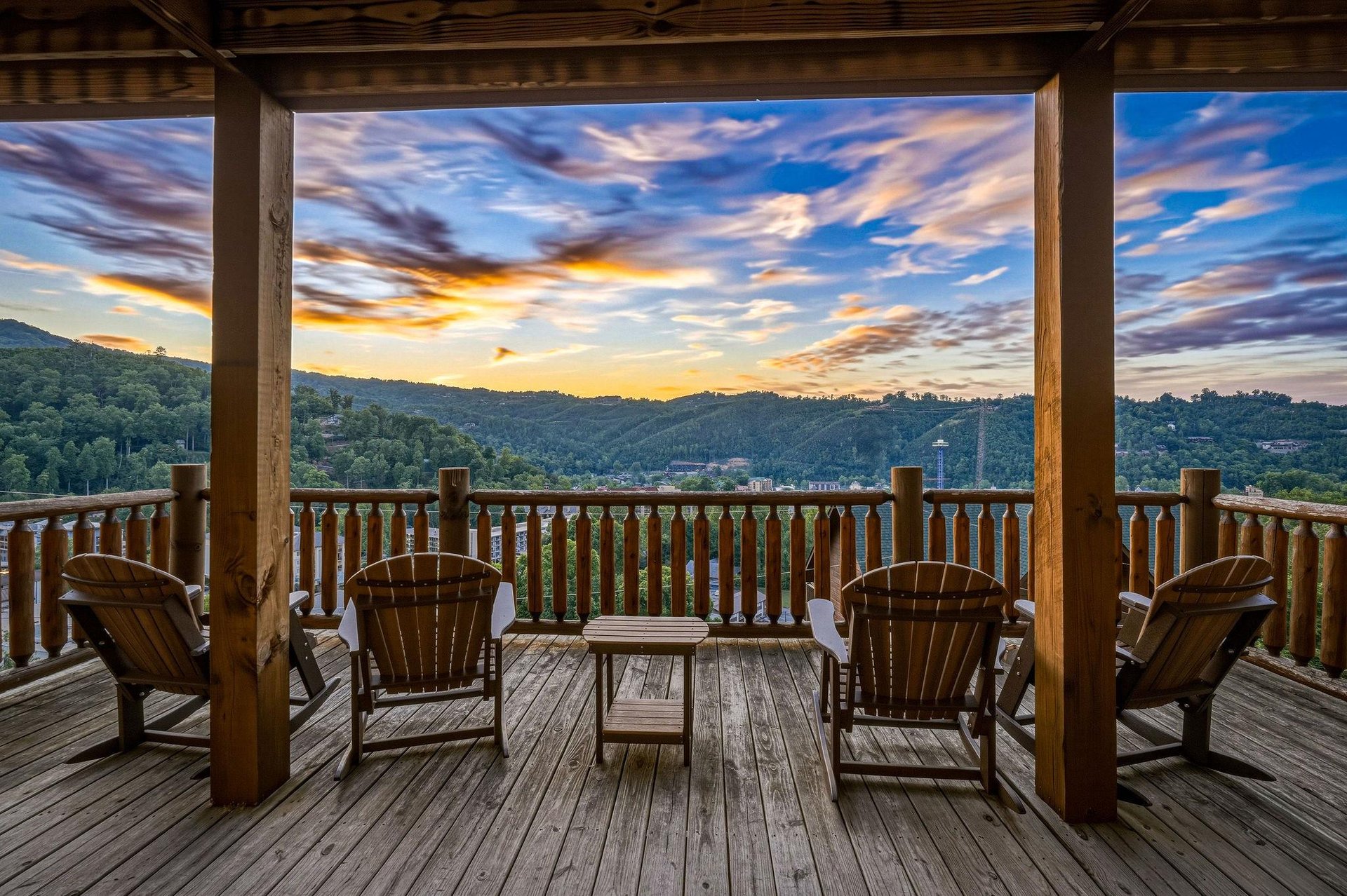 A stunning sunset paints the sky with fiery hues over forested mountains, creating a breathtaking backdrop from this spacious covered deck—perfect for unwinding after a day of adventure.