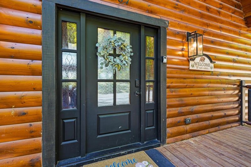 Charming log cabin entrance with elegant black door, decorative wreath, and welcoming touches that greet you upon arrival.