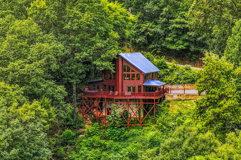 A distinctive red cabin nestled among lush green forest on an elevated deck, offering a peaceful natural setting and unique architecture.