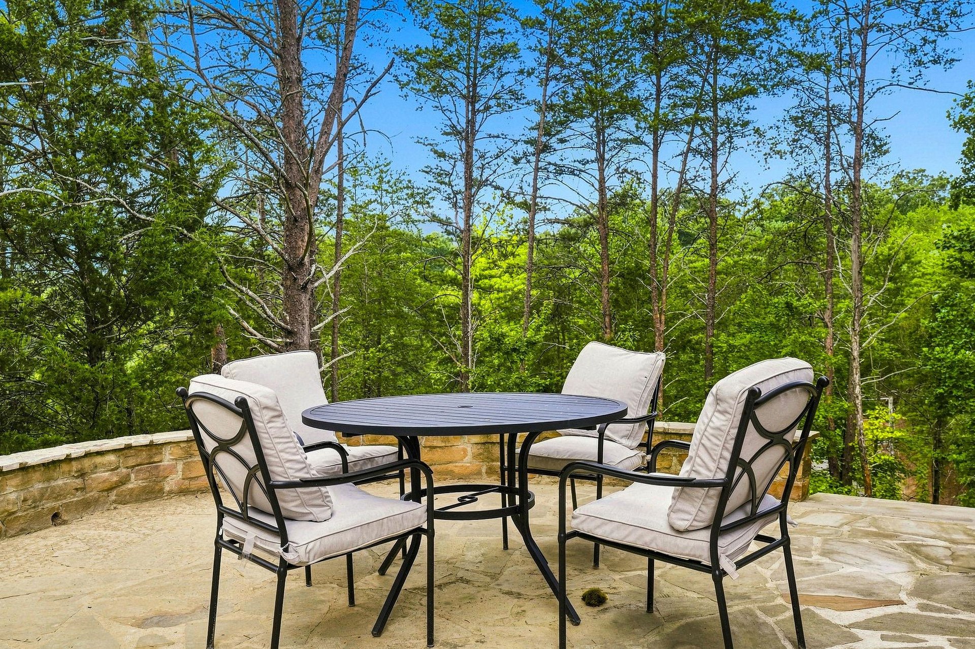 Relax in your private outdoor retreat, where comfortable seating and lush forest views create the perfect spot for morning coffee or evening conversations under a brilliant blue sky.