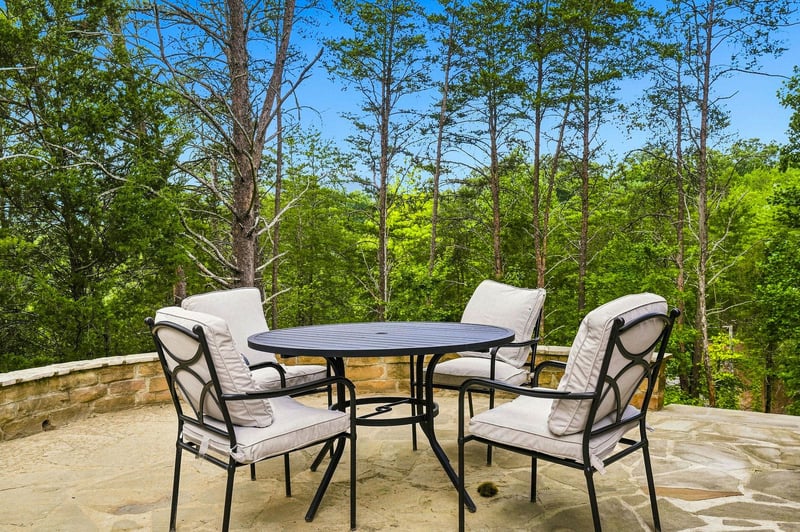 Relax in your private outdoor retreat, where comfortable seating and lush forest views create the perfect spot for morning coffee or evening conversations under a brilliant blue sky.