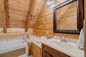 Soak tub with tile and square mirror above single vanity