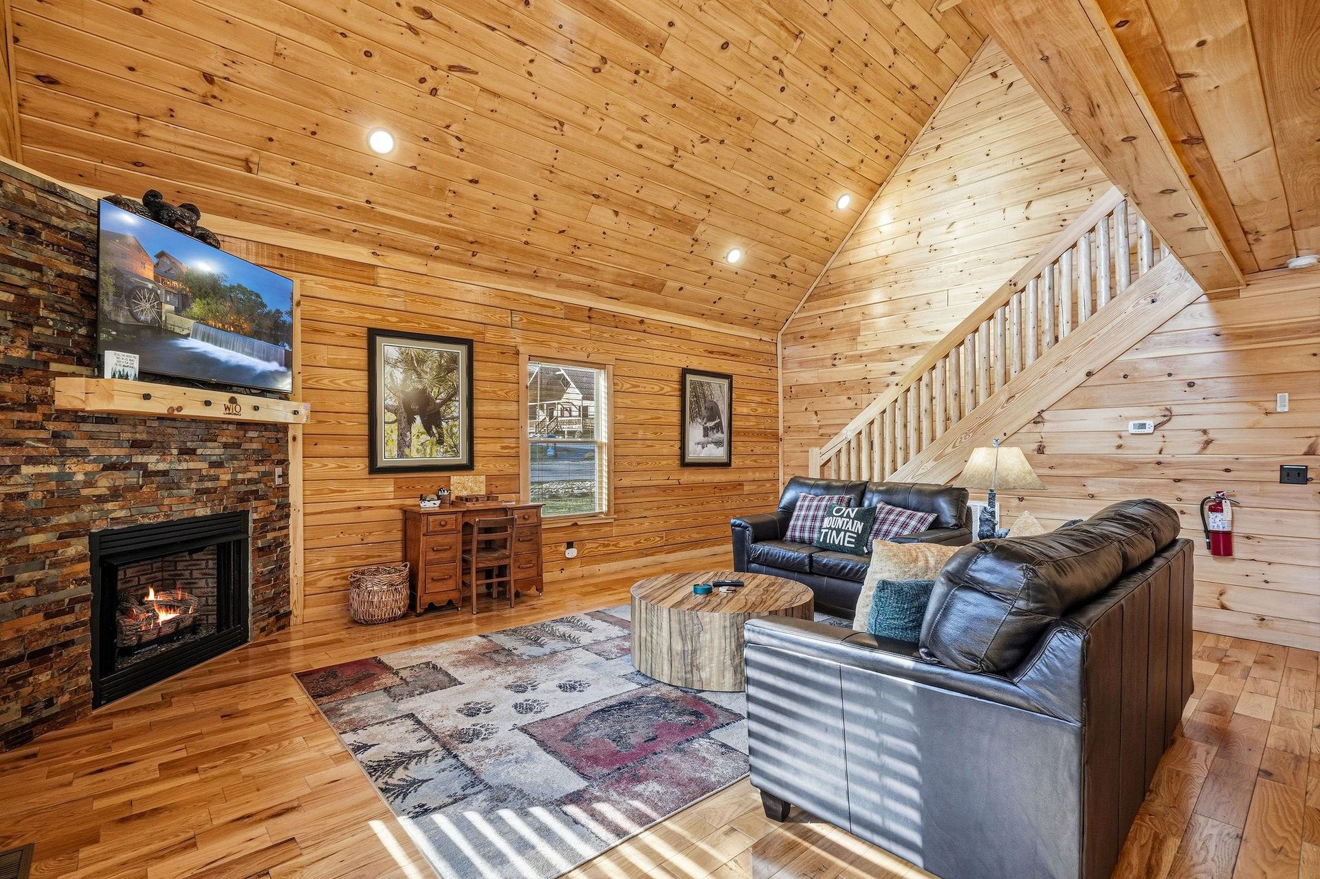 Sink into plush leather seating by your crackling fireplace, where rustic wood walls create the perfect cabin retreat atmosphere.