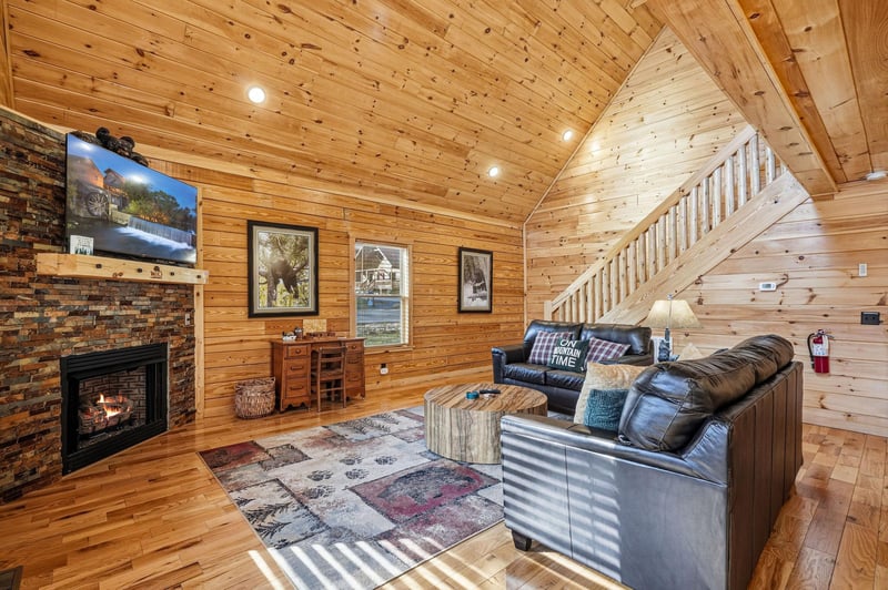 Sink into plush leather seating by your crackling fireplace, where rustic wood walls create the perfect cabin retreat atmosphere.