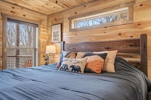 Sink into this rustic bedrooms cozy embrace with its handcrafted wooden headboard, soft linens, and peaceful forest views through your window.