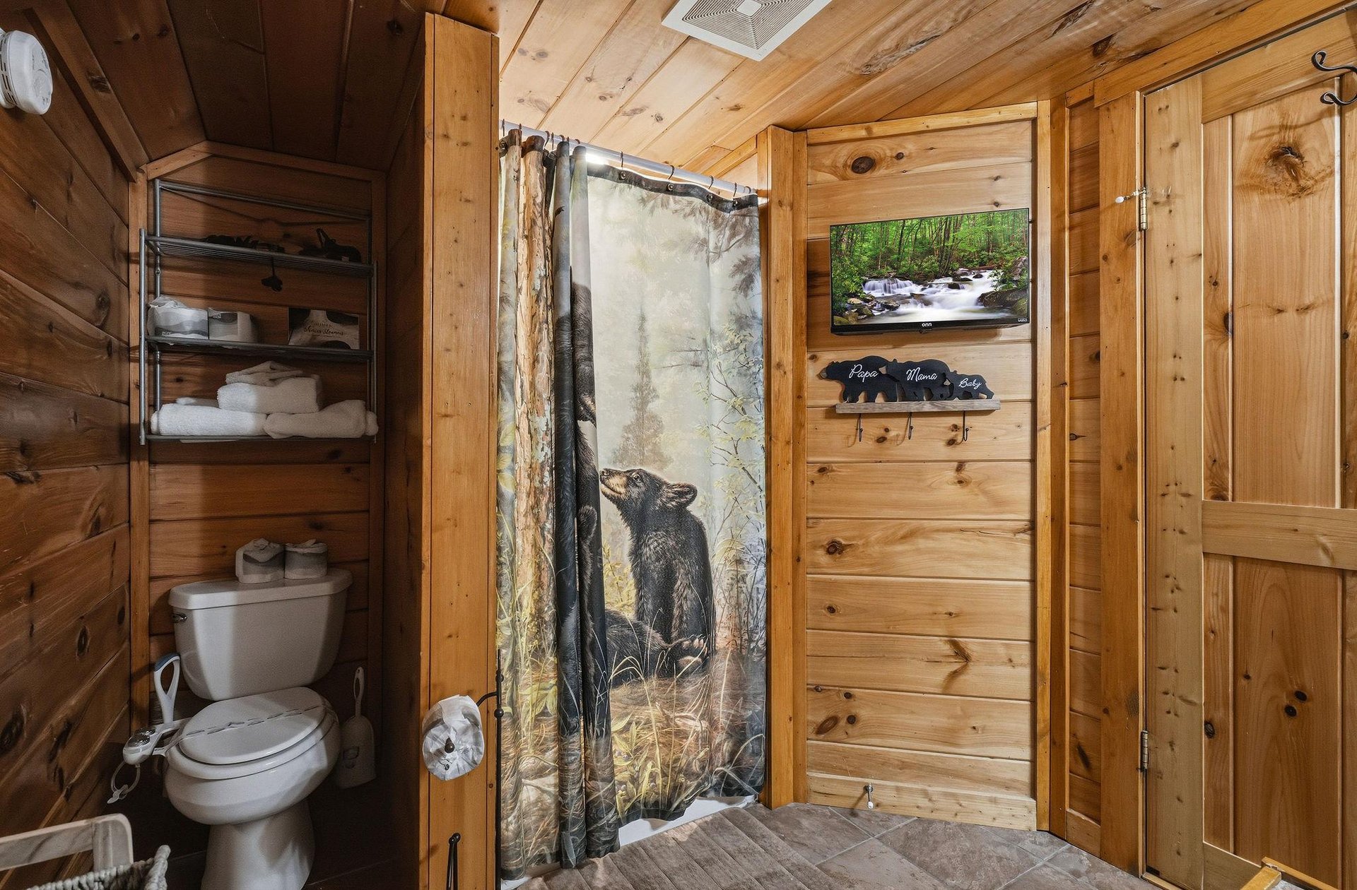 Your private bathroom features warm wood paneling and rustic cabin charm, complete with a cozy bearthemed shower curtain and fresh towels waiting for you.