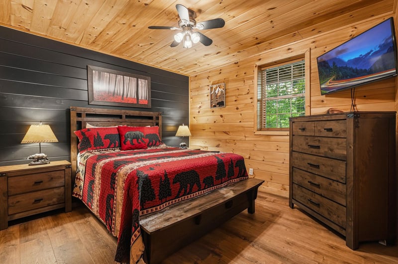 Your cozy cabin bedroom blends rustic pine walls with stylish black shiplap, creating a warm retreat where youll drift off under the glow of bedside lamps and a ceiling fan.