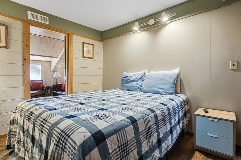 Rest peacefully in your cozy bedroom featuring soft blue plaid bedding and modern track lighting for nighttime reading comfort.