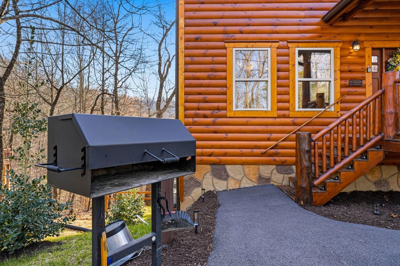 A charming log cabin exterior features a spacious BBQ grill for outdoor cooking adventures surrounded by peaceful forest views.
