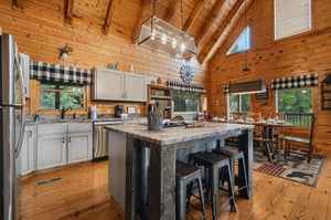 Step into this inviting cabinstyle kitchen with warm wood beams, a granite island perfect for family meals, and large windows framing peaceful forest views.