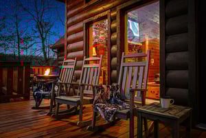 Cozy log cabin porch with rocking chairs and warm lighting creates the perfect evening retreat under starlit skies.