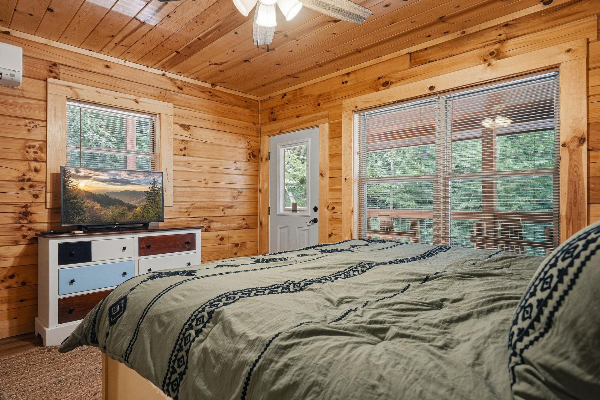 Drift off to sleep in this cozy bedroom where warm wood surrounds you and natural light pours in through large windows, offering peaceful forest views just beyond your bed.
