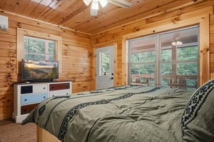 Drift off to sleep in this cozy bedroom where warm wood surrounds you and natural light pours in through large windows, offering peaceful forest views just beyond your bed.