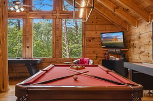 Your own game room features a fullsize pool table and arcade fun, framed by towering windows that bring the forest inside—perfect for friendly competition surrounded by nature.