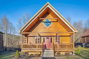 Charming log cabin featuring warm wood construction, welcoming front porch, and distinctive blue diamond window accent in peaceful mountain setting.