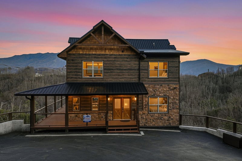 Mountain cabin with stone and wood exterior under vibrant sunset skies, surrounded by rolling hills and natural landscape.