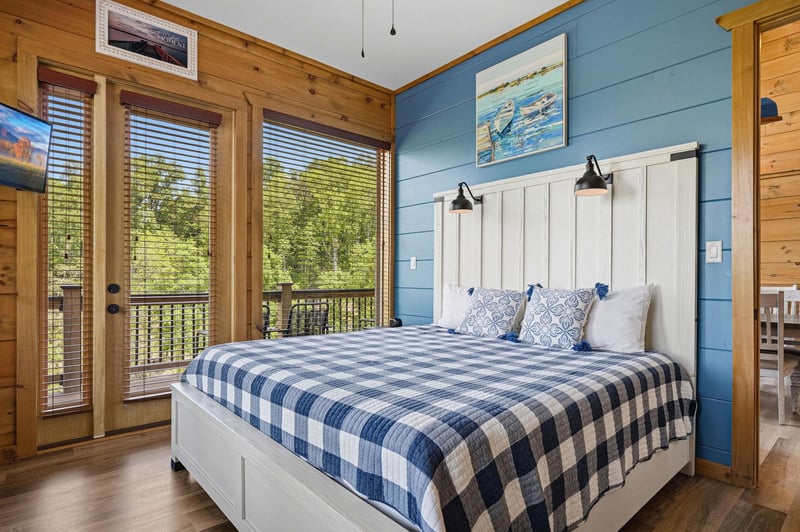 Wake up to forest views streaming through your private balcony doors in this cozy blue and white bedroom retreat.