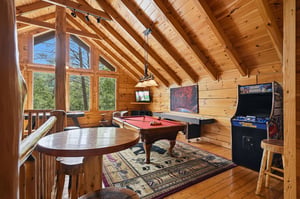Your private game room awaits with vaulted wood ceilings, a pool table, arcade games, and stunning forest views—perfect for unwinding and playing after a day of adventure.
