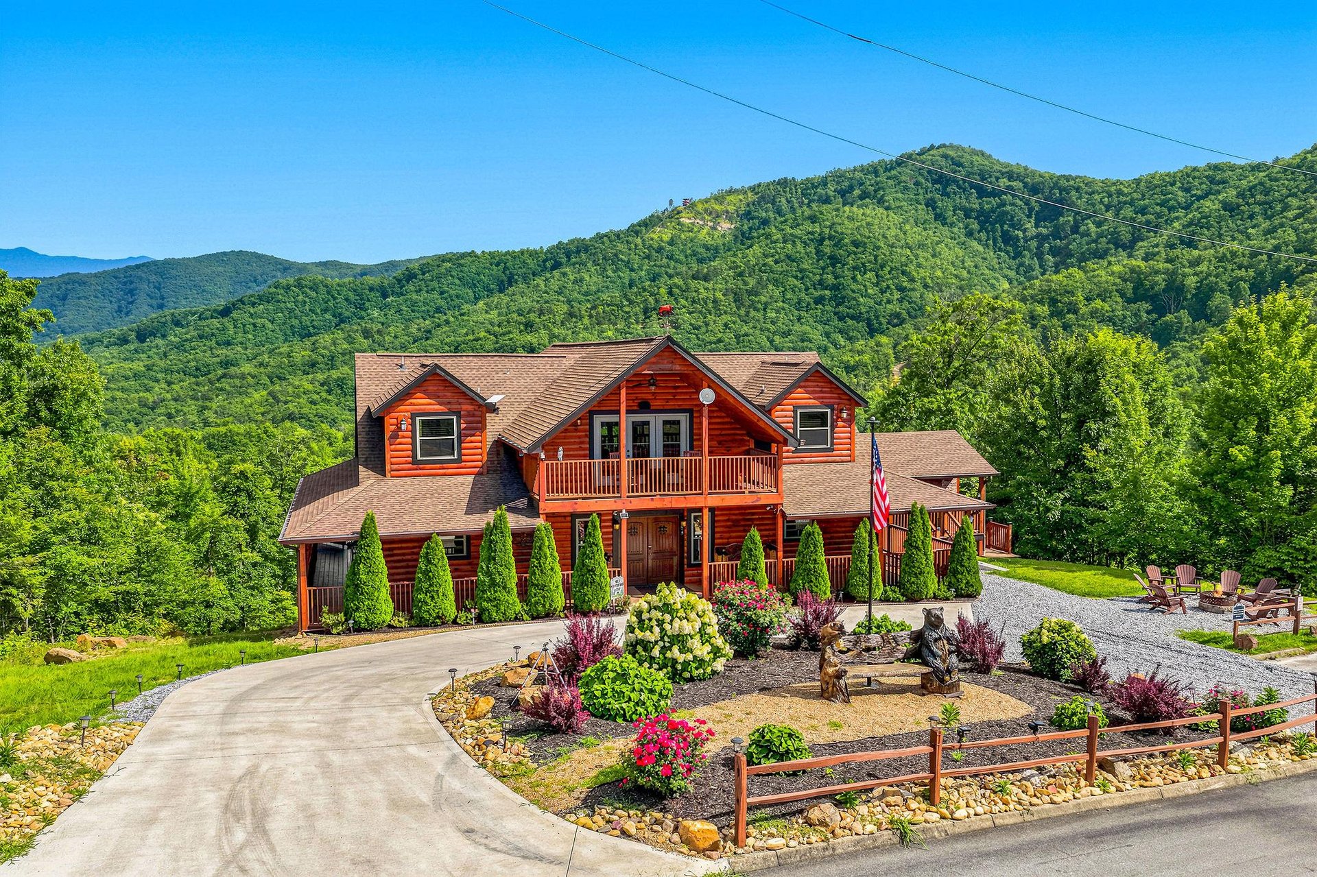A welcoming mountain retreat with timber architecture, nestled against lush green hillsides. Manicured gardens, curving driveway, and panoramic views create a peaceful vacation setting.