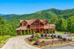 A welcoming mountain retreat with timber architecture, nestled against lush green hillsides. Manicured gardens, curving driveway, and panoramic views create a peaceful vacation setting.