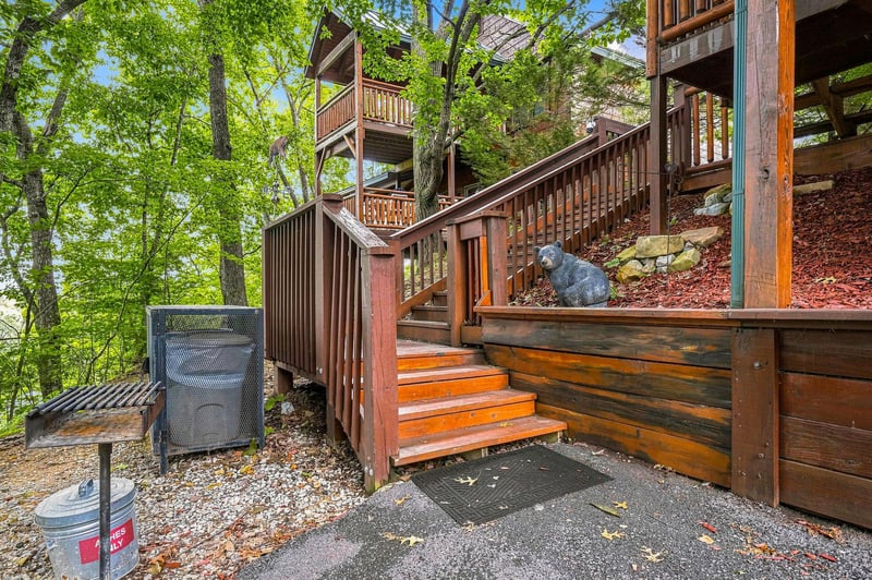 Multilevel wooden cabin nestled in lush forest with outdoor grilling area and rustic woodland charm.