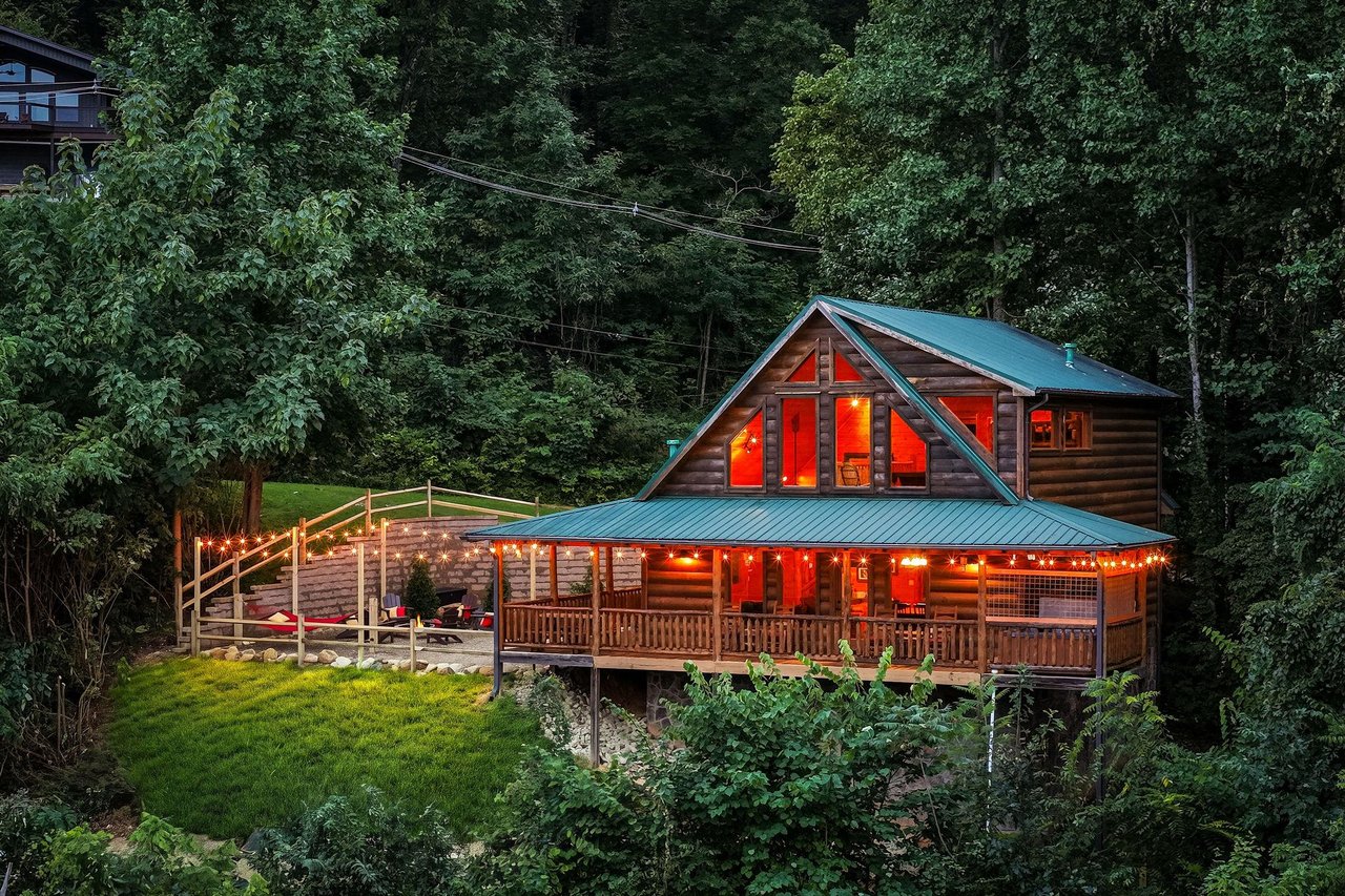 A secluded log cabin surrounded by towering trees in a lush forest setting, offering a peaceful mountain retreat with warm lighting and spacious decks for outdoor relaxation.