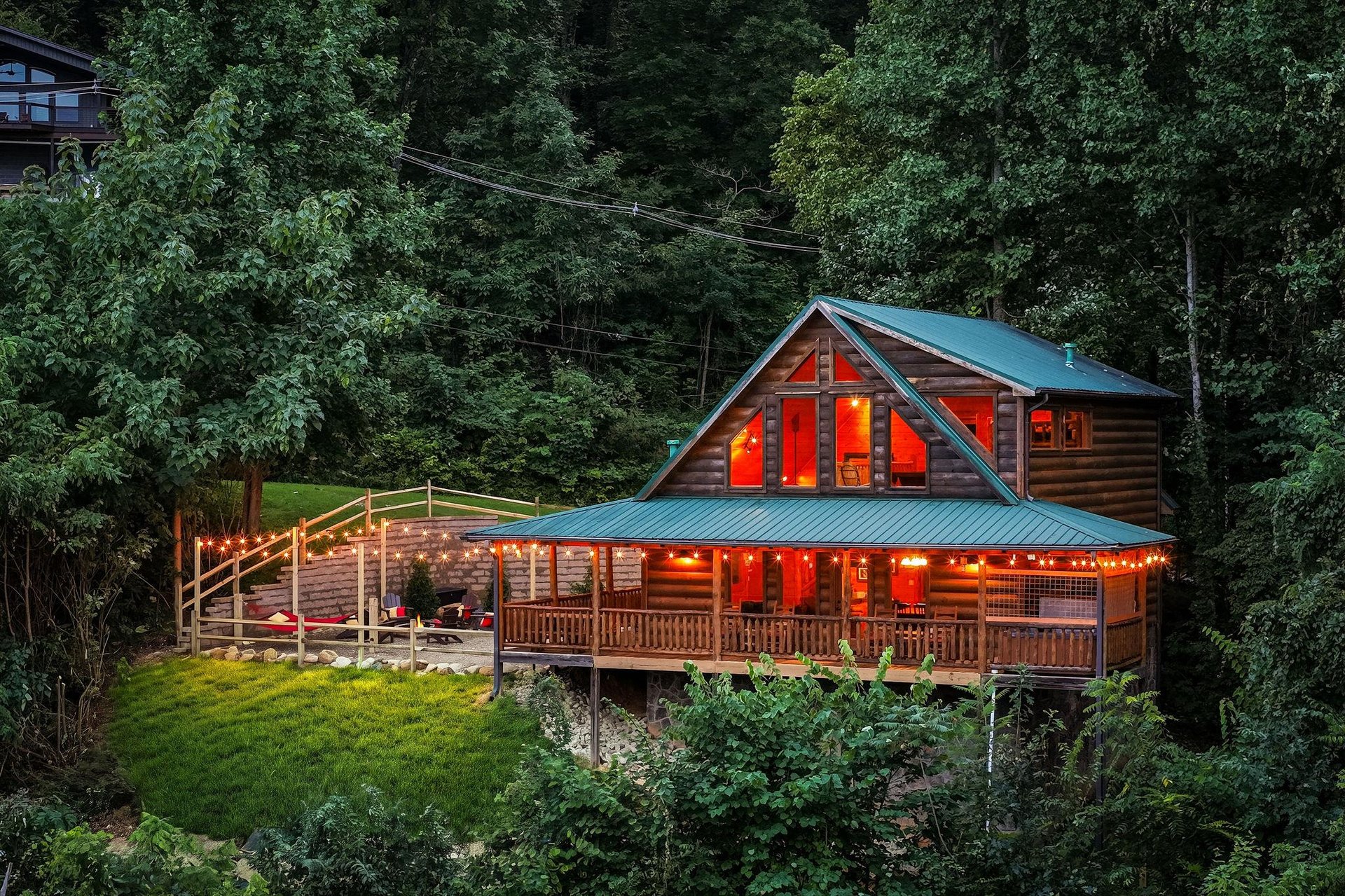 A secluded log cabin surrounded by towering trees in a lush forest setting, offering a peaceful mountain retreat with warm lighting and spacious decks for outdoor relaxation.