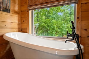 Sink into this inviting soaking tub surrounded by warm wood and a stunning view of lush greenery just beyond the window—your perfect escape.