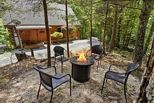 A cozy log cabin nestled among towering pines, with a fire pit and seating area where you can gather under the trees and enjoy peaceful forest views.