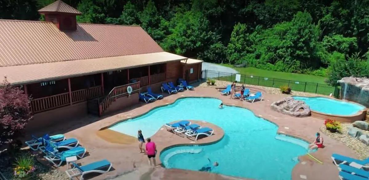 Expansive pool complex with curved design, surrounded by lush forest and featuring multiple swimming areas for endless summer fun.