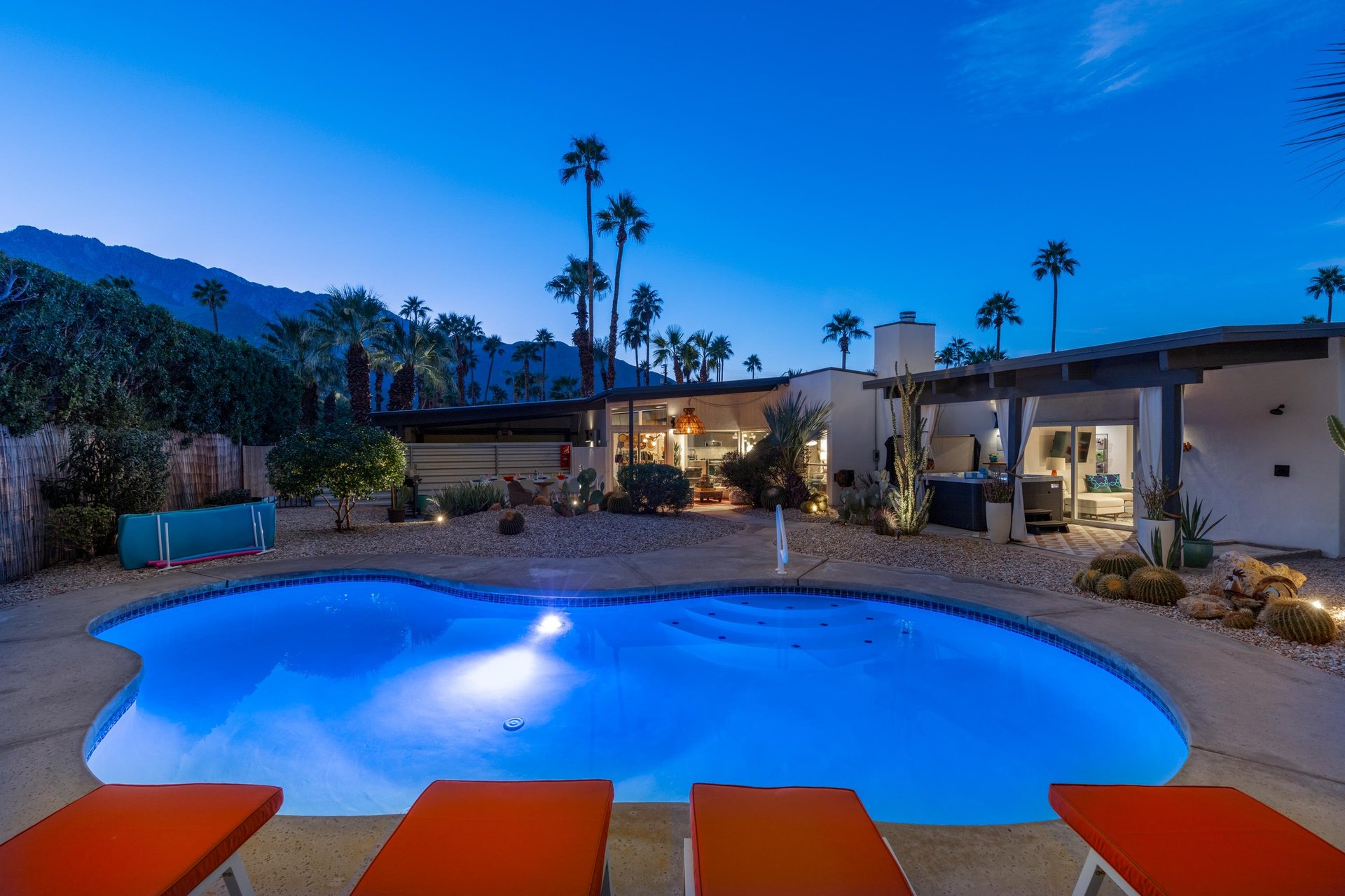 Modern desert retreat features illuminated pool surrounded by iconic palms and mountain backdrop.